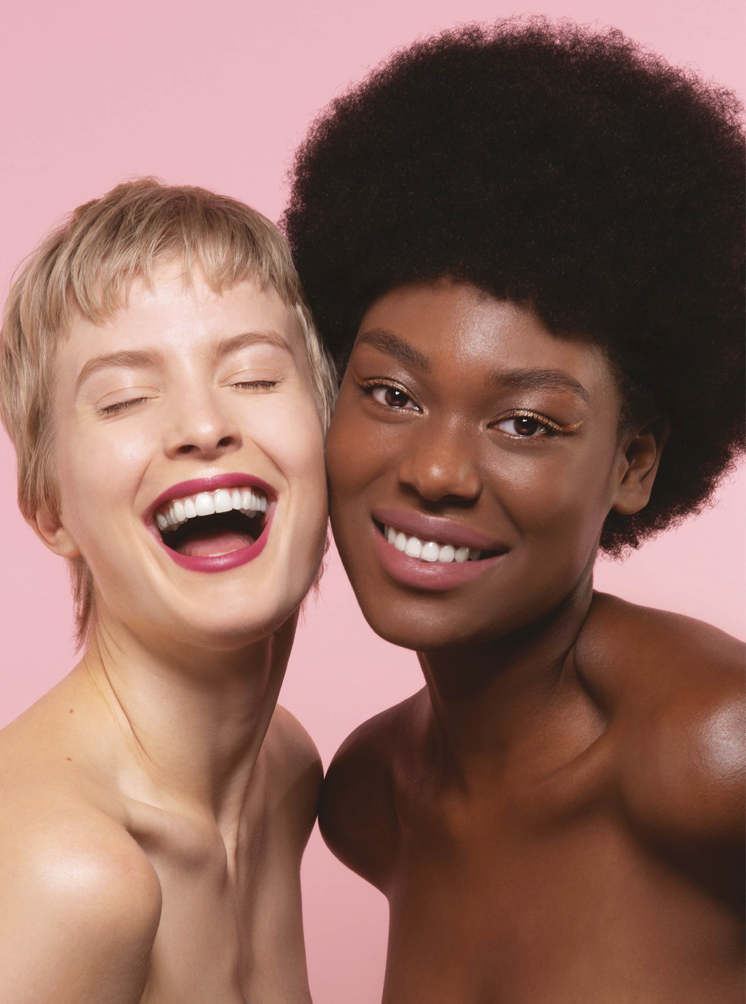 Two women laughing together on a pink background